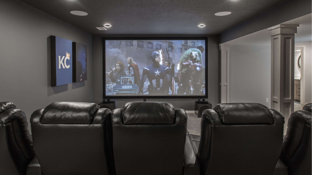 A home theatre with leather seats and a screen showing a superhero movie after a basement finish in Shawnee, KS