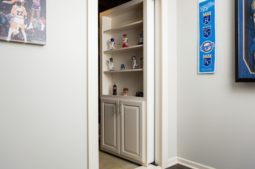 a secret door created as part of a custom home remodel in Shawnee that is concealed as a bookshelf displaying collectables opens to a room
