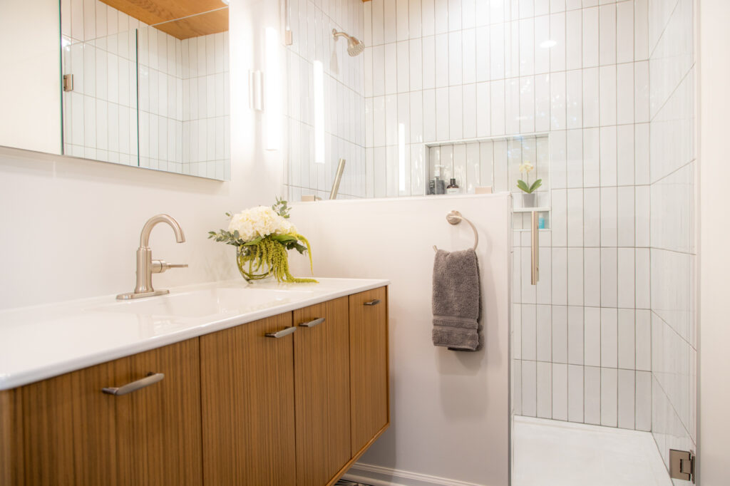 a bathroom remodel in Leawood showcasing natural wood counters and LED light illuminating the white-tiled shower