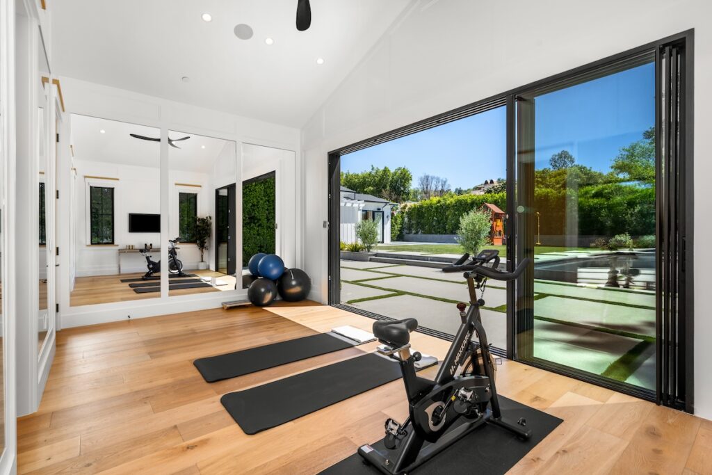 a luxurious home gym with wood floors and cycling equipment in front of windows that Shack Built's basement contractors in Leawood can design and build